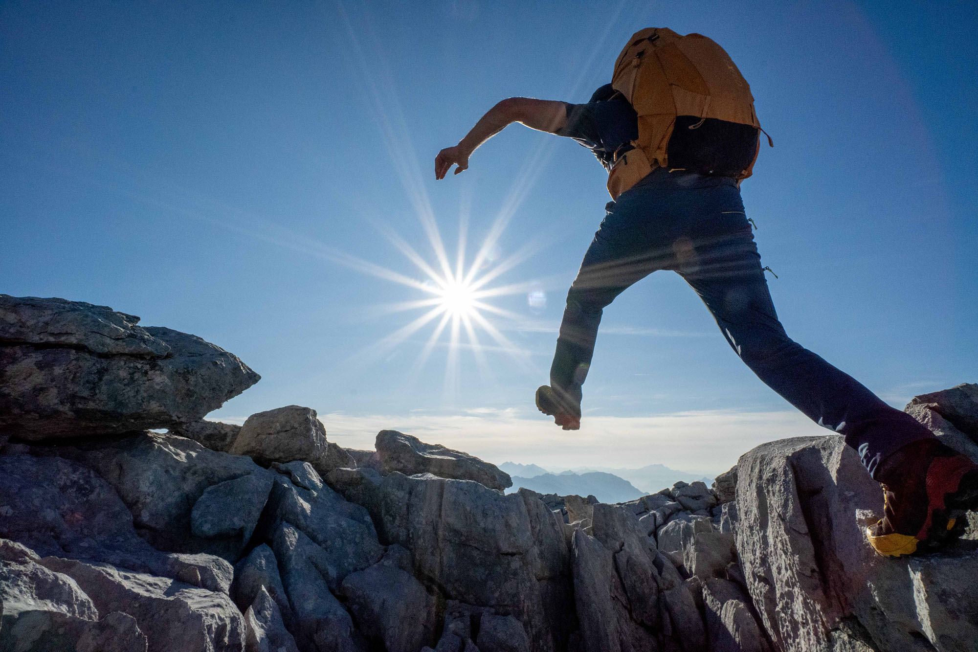 hiker jumping over canyon with rising sun