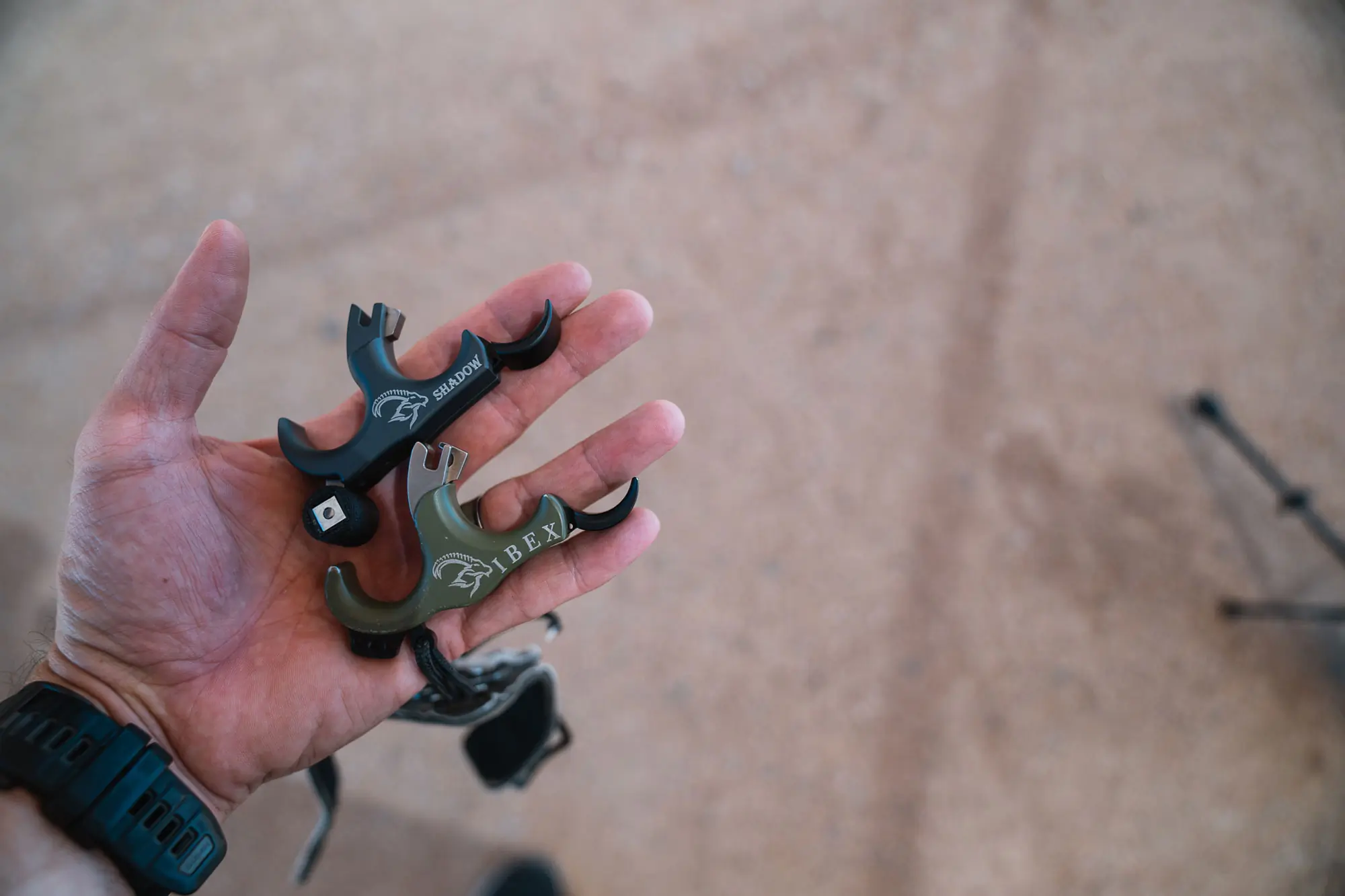 A hand holding two archery Review Evolution Outdoors Shadow Thumb Button Releases