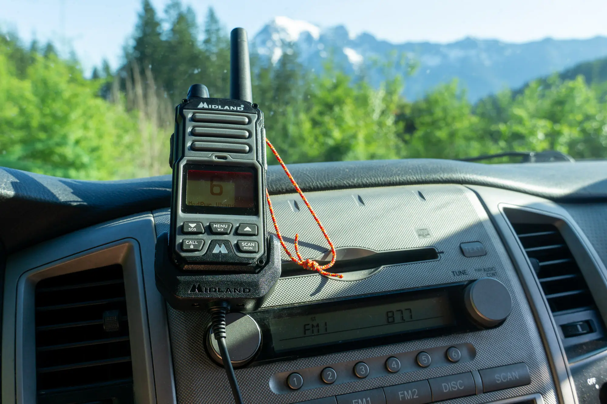 the gxt67 radio sits on the dash of a truck, looking over a forest and mountain