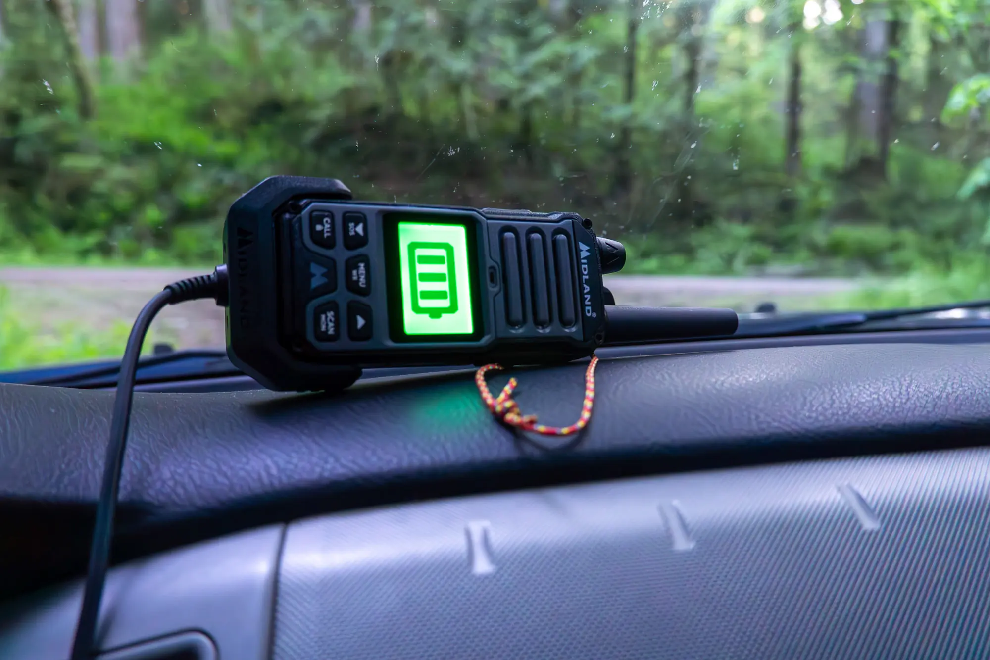 the gxt67 radio sits on the dash of a truck while recharging with the included vehicle charger