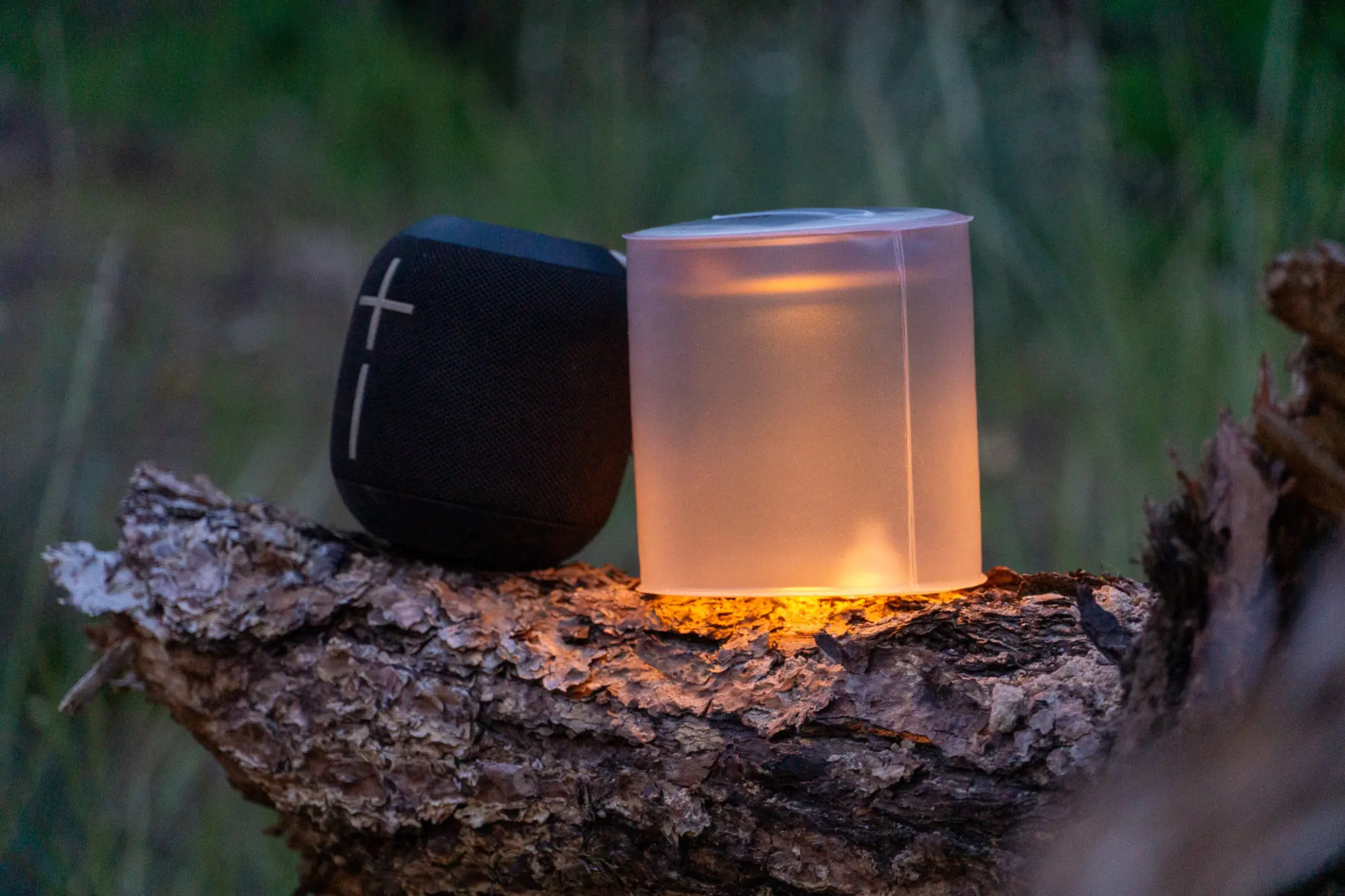 the biolite luci candle lantern flickers dimly beside a speaker while sitting on a log
