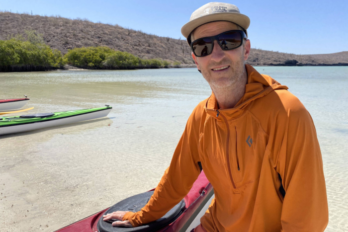 Man at the beach wearing sunglasses and Black Diamond Alpenglow Pro Hoody