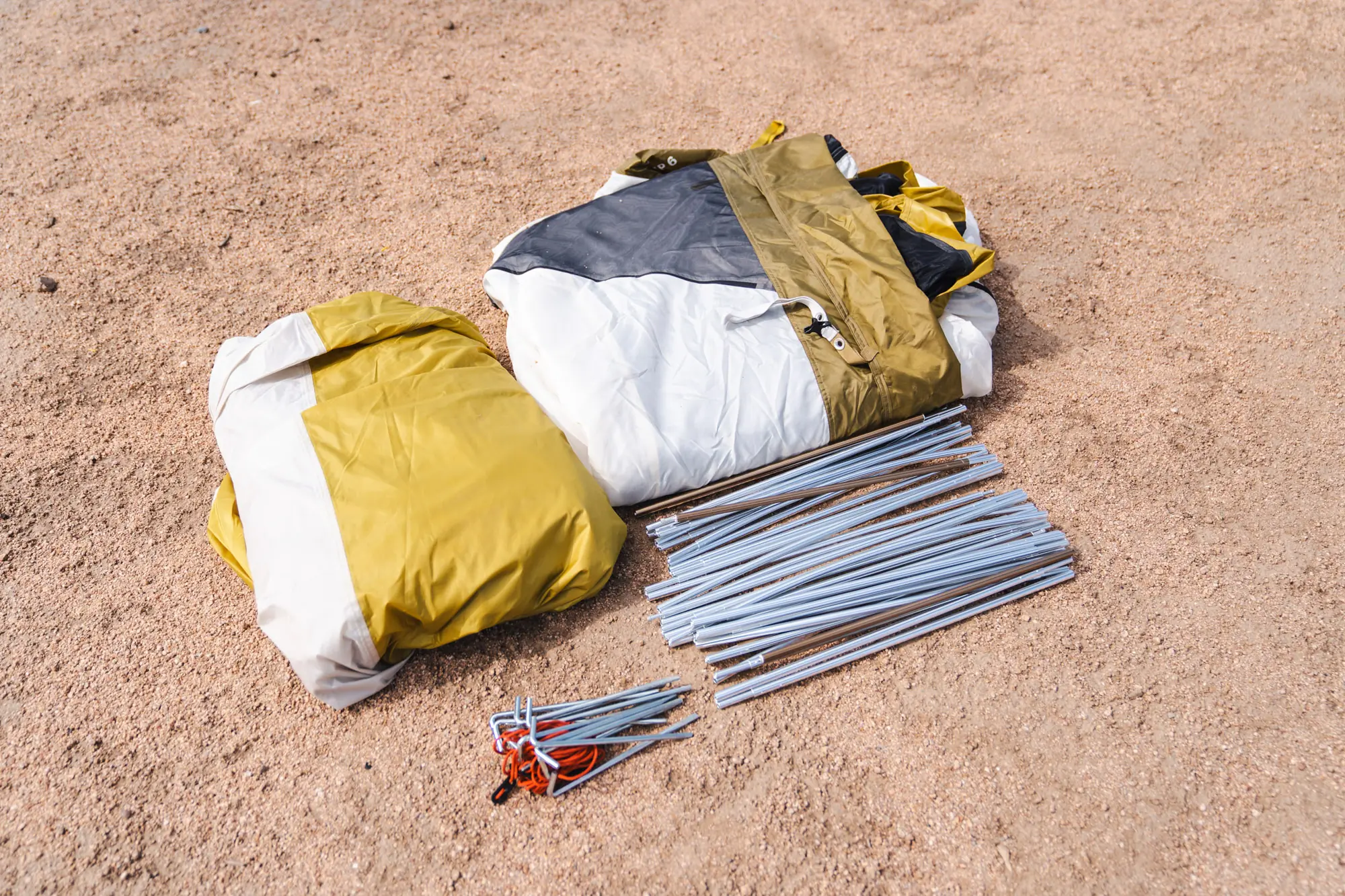 the base camp 6 tent and vehicle connector components lay on a sandy soil in colorado