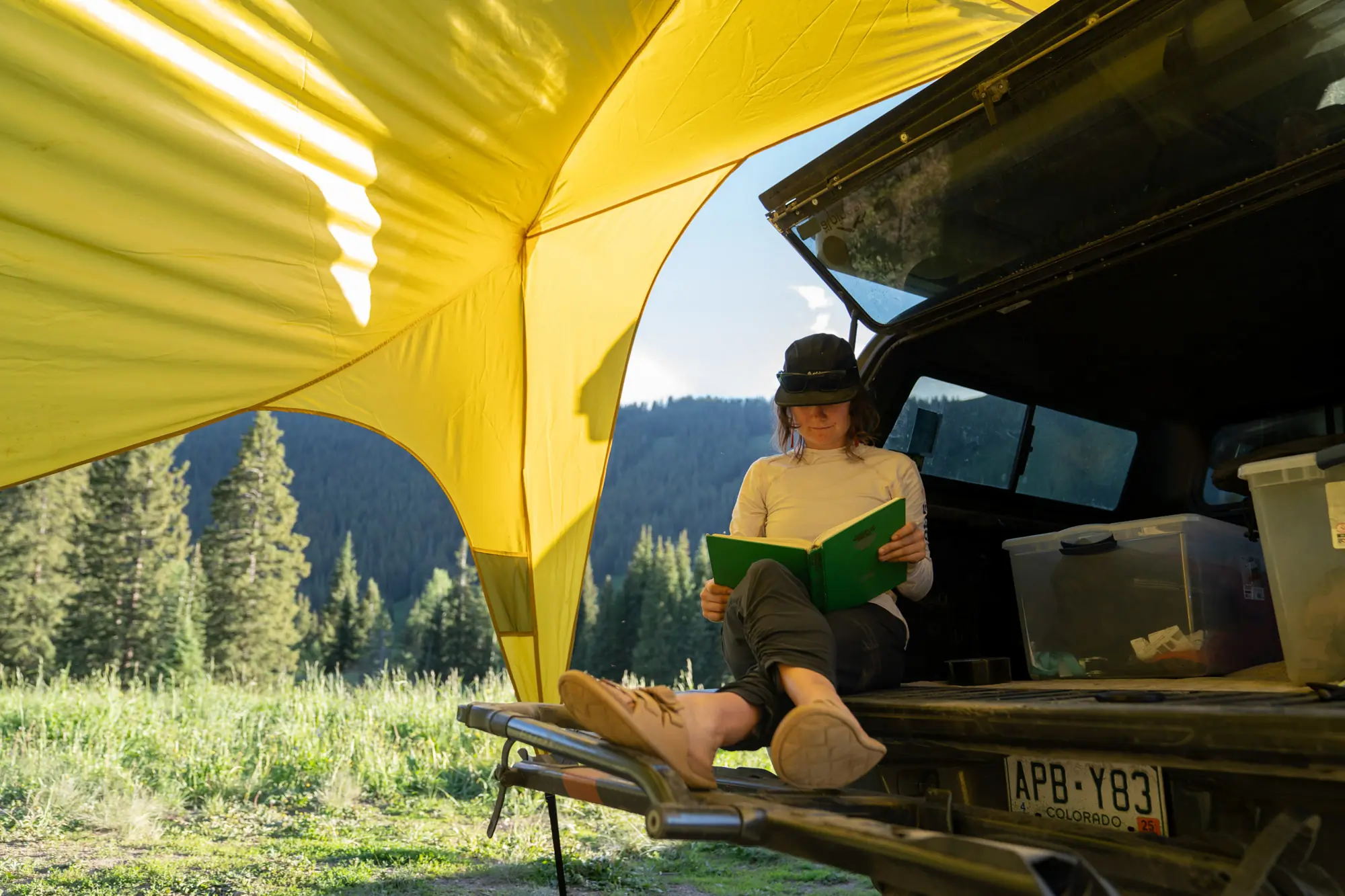 the author reads a book in the back of her truck, shaded by the base camp vehicle connector