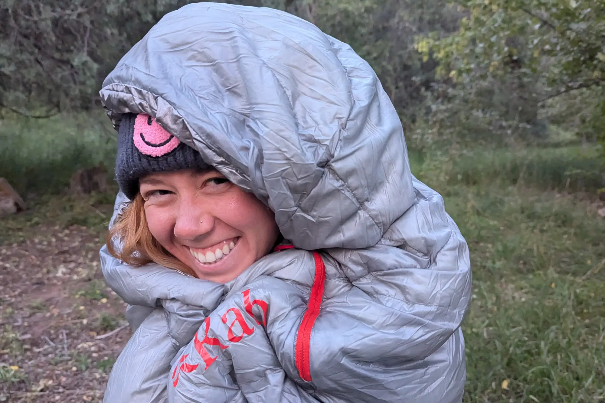 a camper tucks into the mythic ultra sleeping bag, wearing it around camp