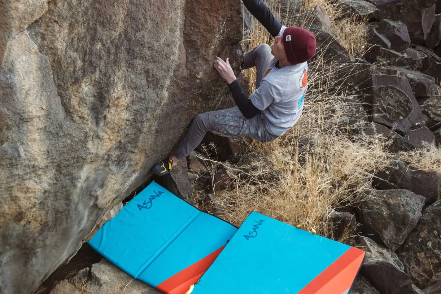 Boulderer climbing above two Asana crashpads. 