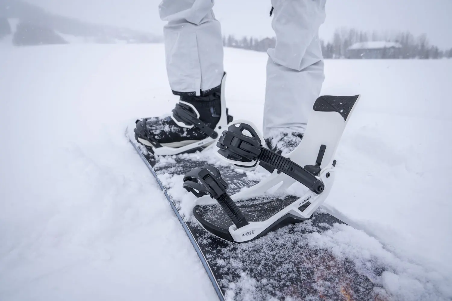 Close-up of snowboard boots strapped into white Jones Mercury FASE snowboard bindings