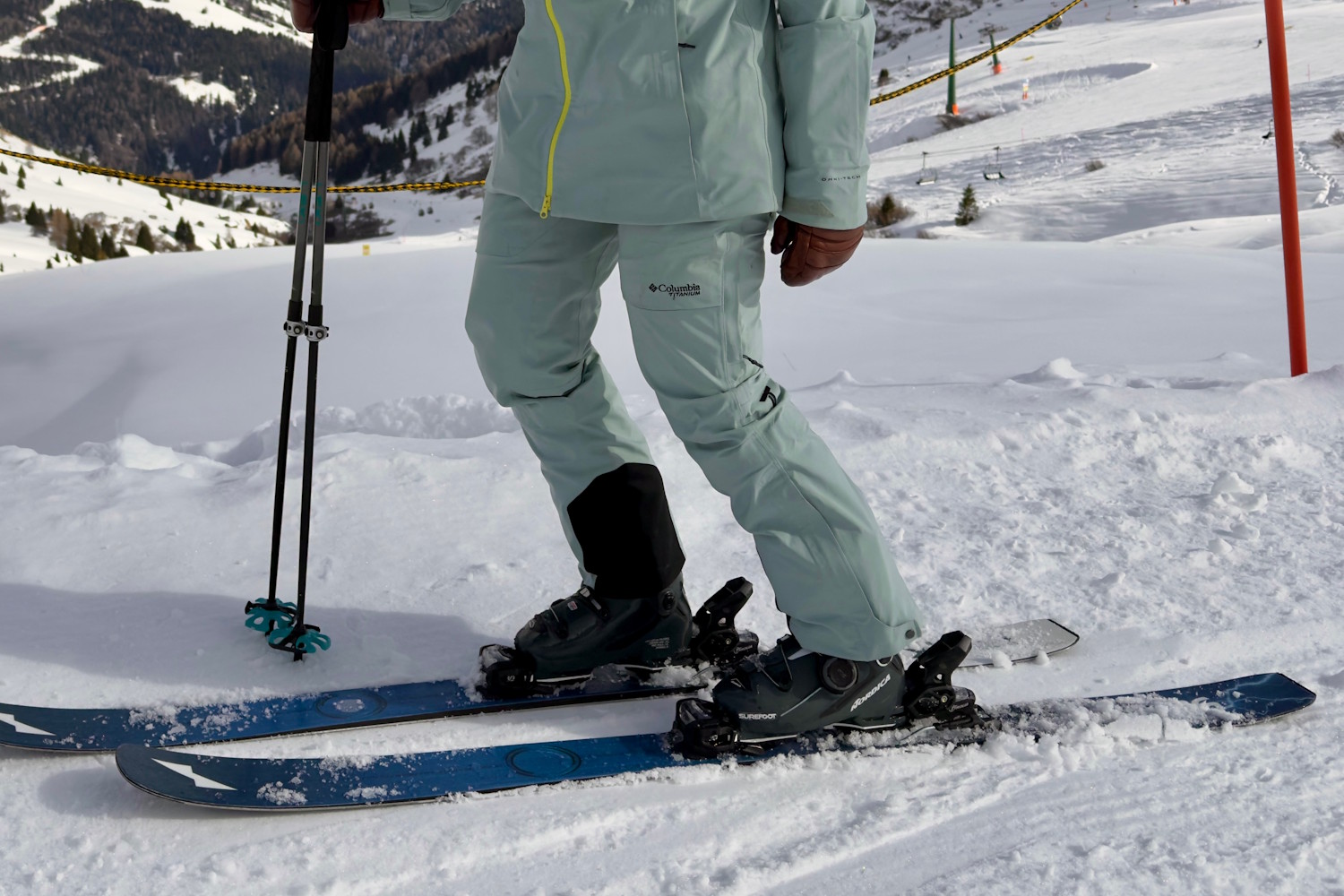 Close-up of a skier wearing Columbia Platinum Peak II pants standing on snow-covered terrain with skis and poles