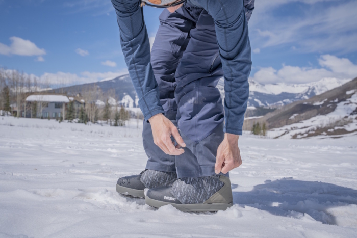 A person in Flylow Stash Bib pants adjusts the cuff over a pair of ThirtyTwo winter boots