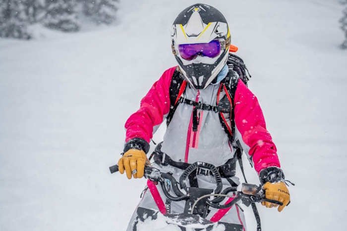 Rider gripping snowmobile handlebars wearing Flylow Super D Ski Gloves in snowy conditions.