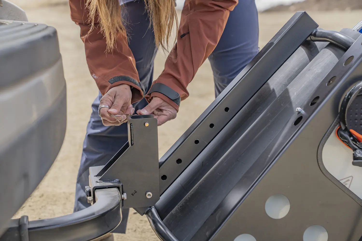 Person installs the Gravirax GR-4 hitch-mounted ski and snowboard rack using a locking pin.