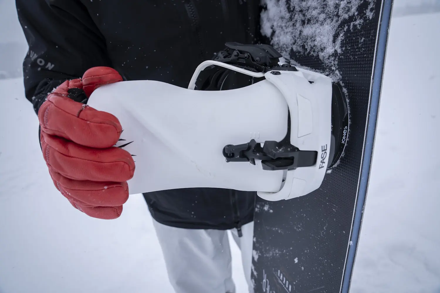 Close-up of a snowboarder securing a white boot into a Jones Mercury FASE snowboard binding