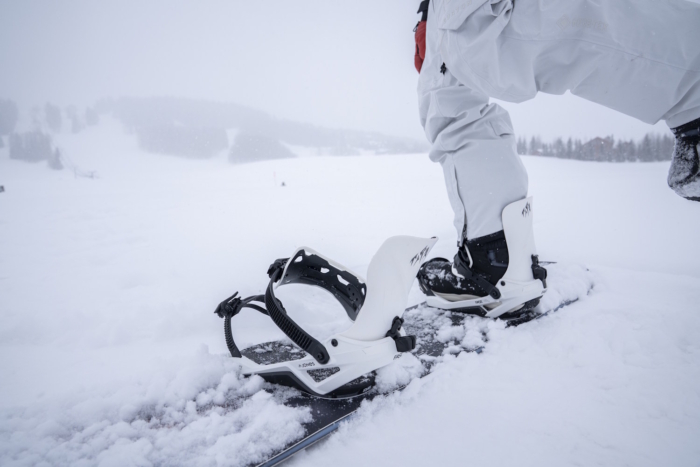 Snowboarder kneeling on a snowy slope with one boot secured in a Jones Mercury FASE binding