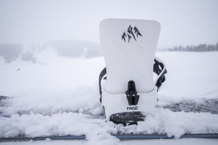Rear view of a white Jones Mercury FASE snowboard binding mounted on a snowboard in fresh snow.