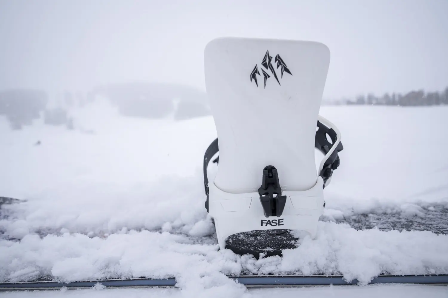 Rear view of a white Jones Mercury FASE snowboard binding mounted on a snowboard in fresh snow.
