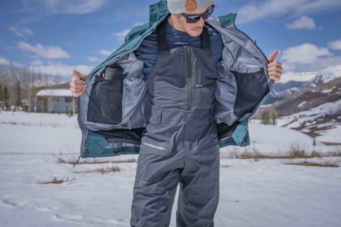 Person opening their jacket to reveal the chest pockets and suspenders of the Jones Shralpinist Recycled GORE-TEX Bibs