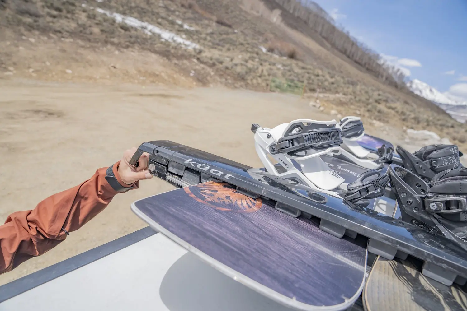 A person secures two snowboards into a Kuat Grip 6 Ski/Snowboard Rack mounted on a vehicle