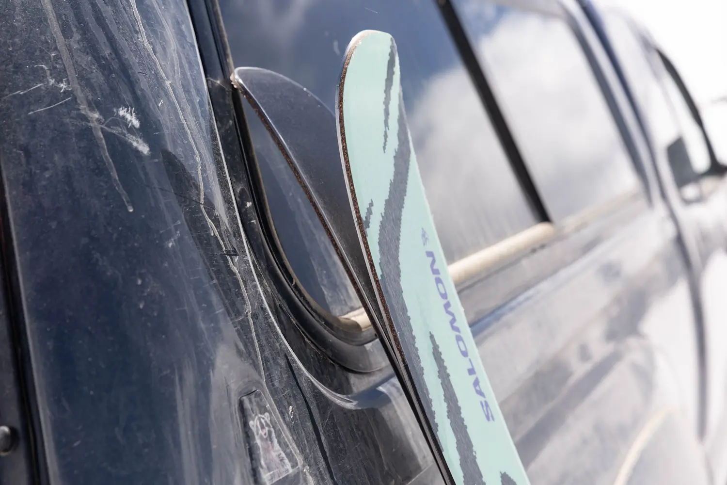 Close-up of Salomon QST 94 skis leaning against a dusty black truck.
