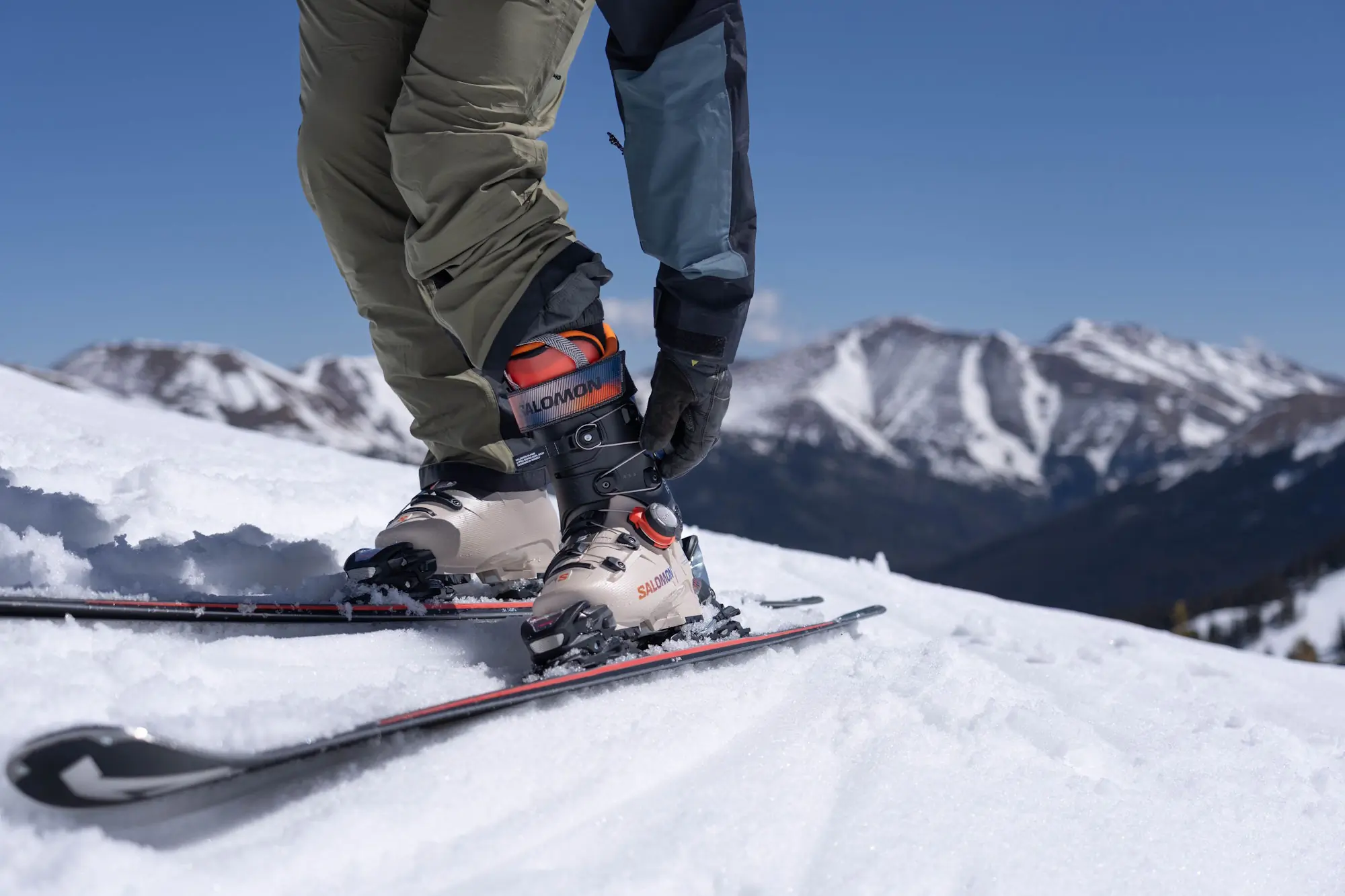 Skier adjusting the Dual BOA dial on Salomon S/Pro Supra 120 Ski Boots on a snowy mountain slope