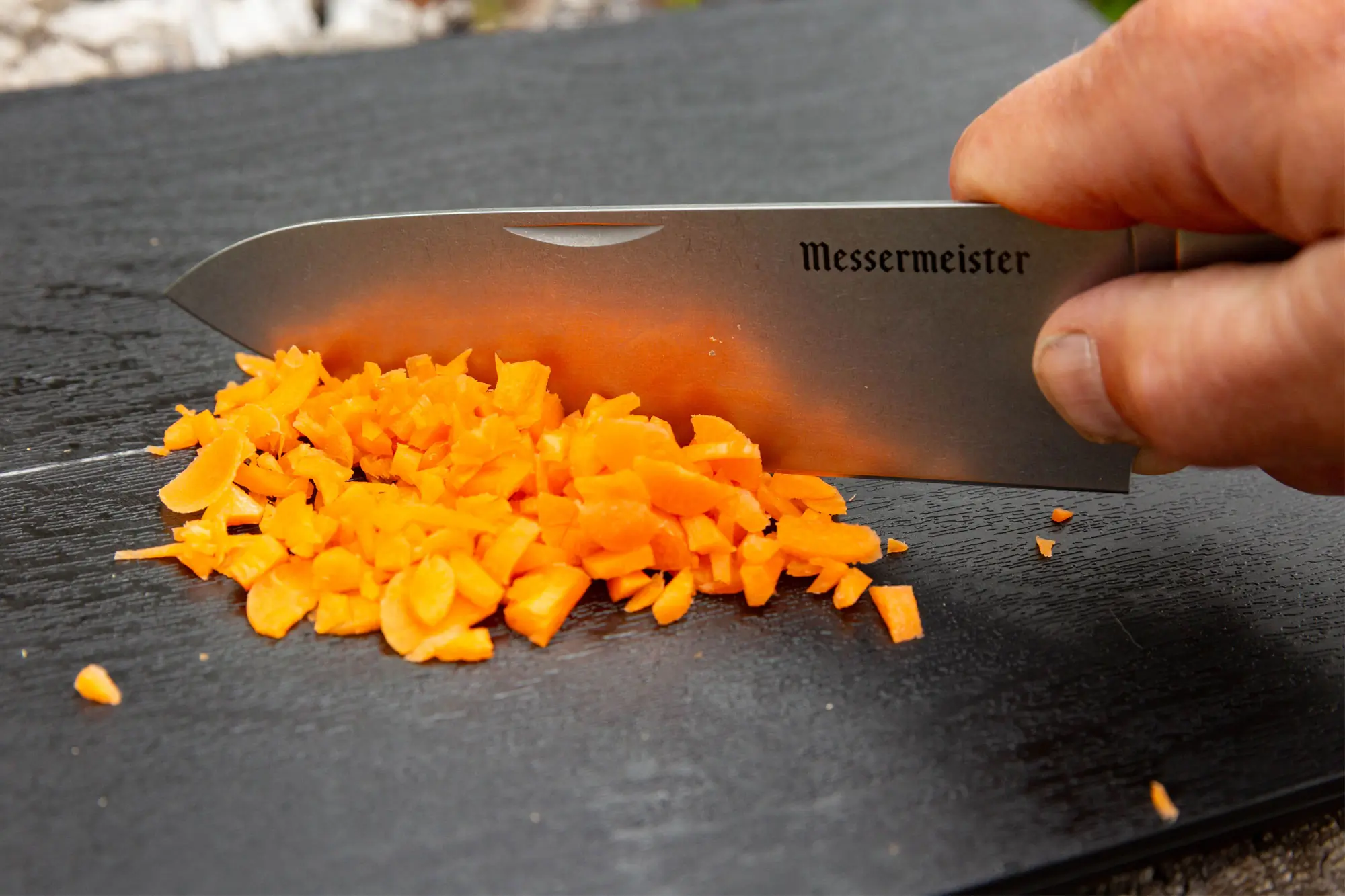 A hand chopping carrots with a Messermeister Adventure Chef Knife