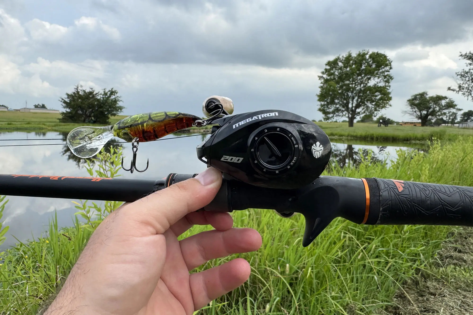 Close-up of a hand holding a KastKing Megatron 200 baitcasting reel with a lure attached
