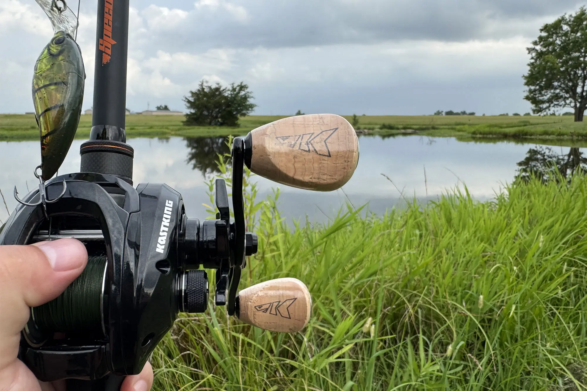 Close-up of a hand holding a baitcasting fishing reel with a crankbait lure