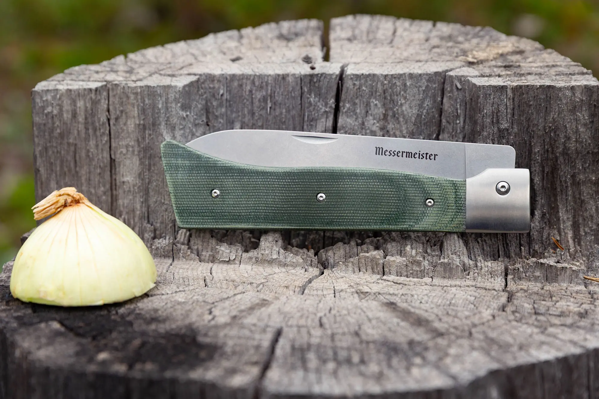 Closed Messermeister Adventure Chef Knife on a tree stump next to a yellow onion