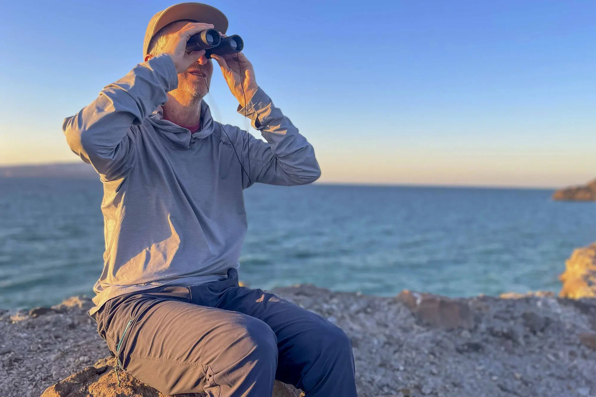 Hiker sitting on a rock and looking through binoculars, wearing REI Co-op Trailmade Pants