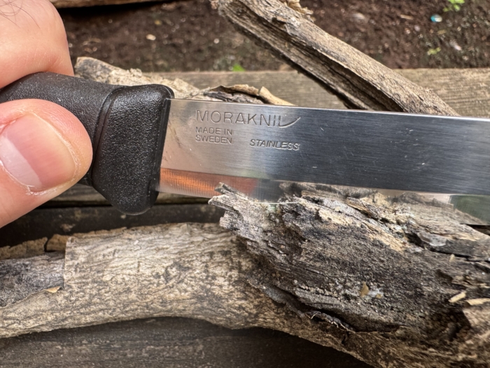 The Morakniv Companion held in a hand, paused as it slices off a piece of a branch.