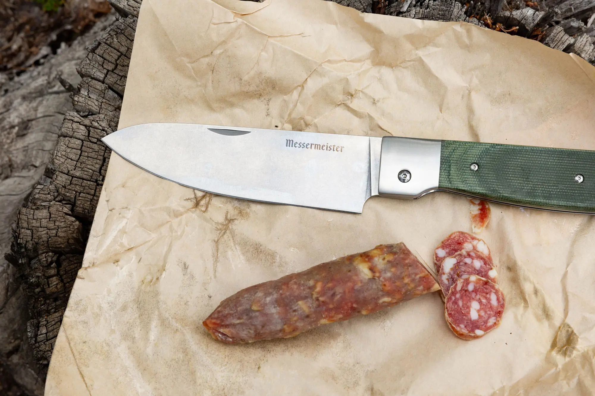 Open Messermeister Adventure Chef Knife on paper next to a piece of sausage
