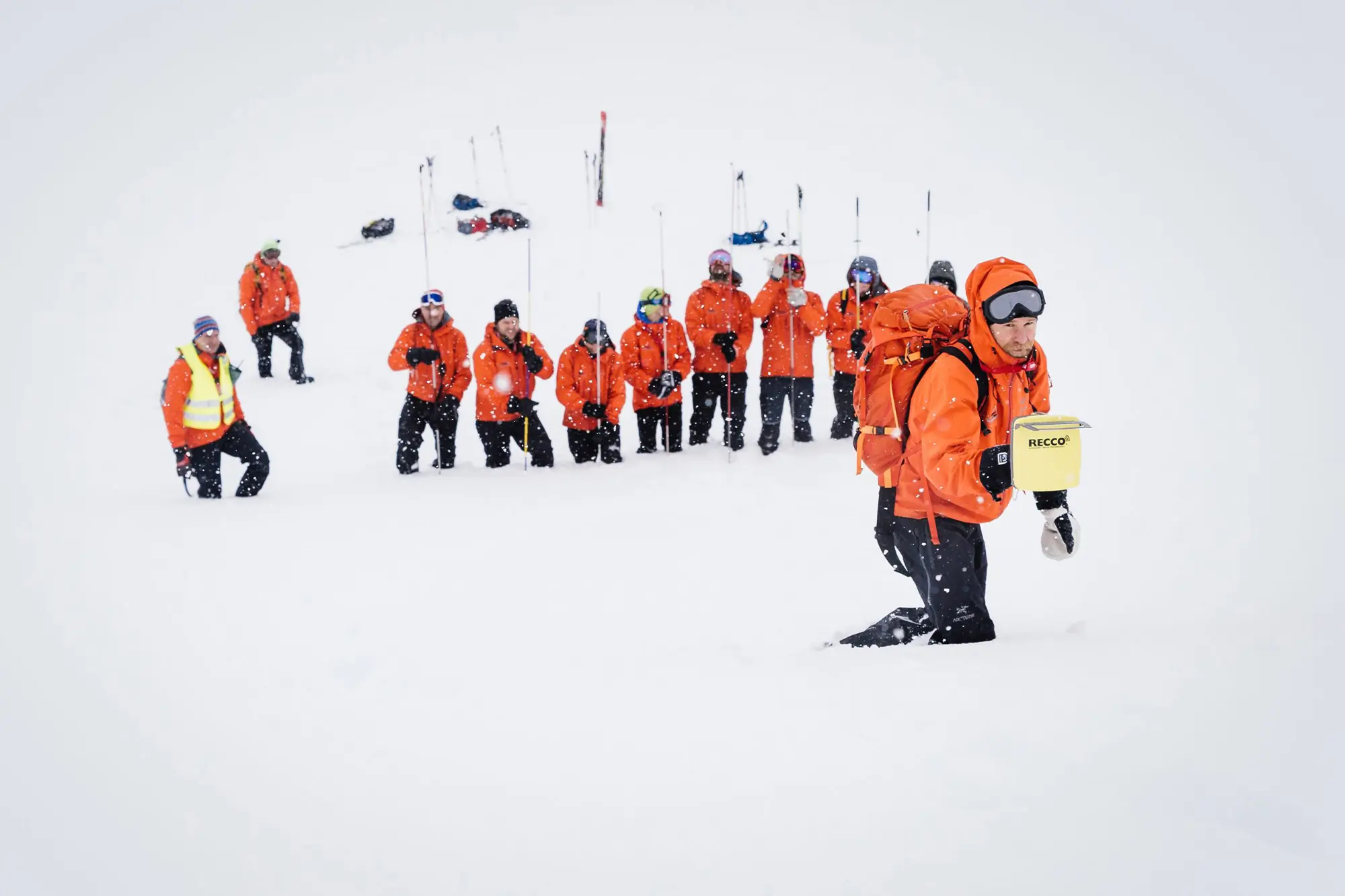 A rescuer walks through deep snow carrying a RECCO device