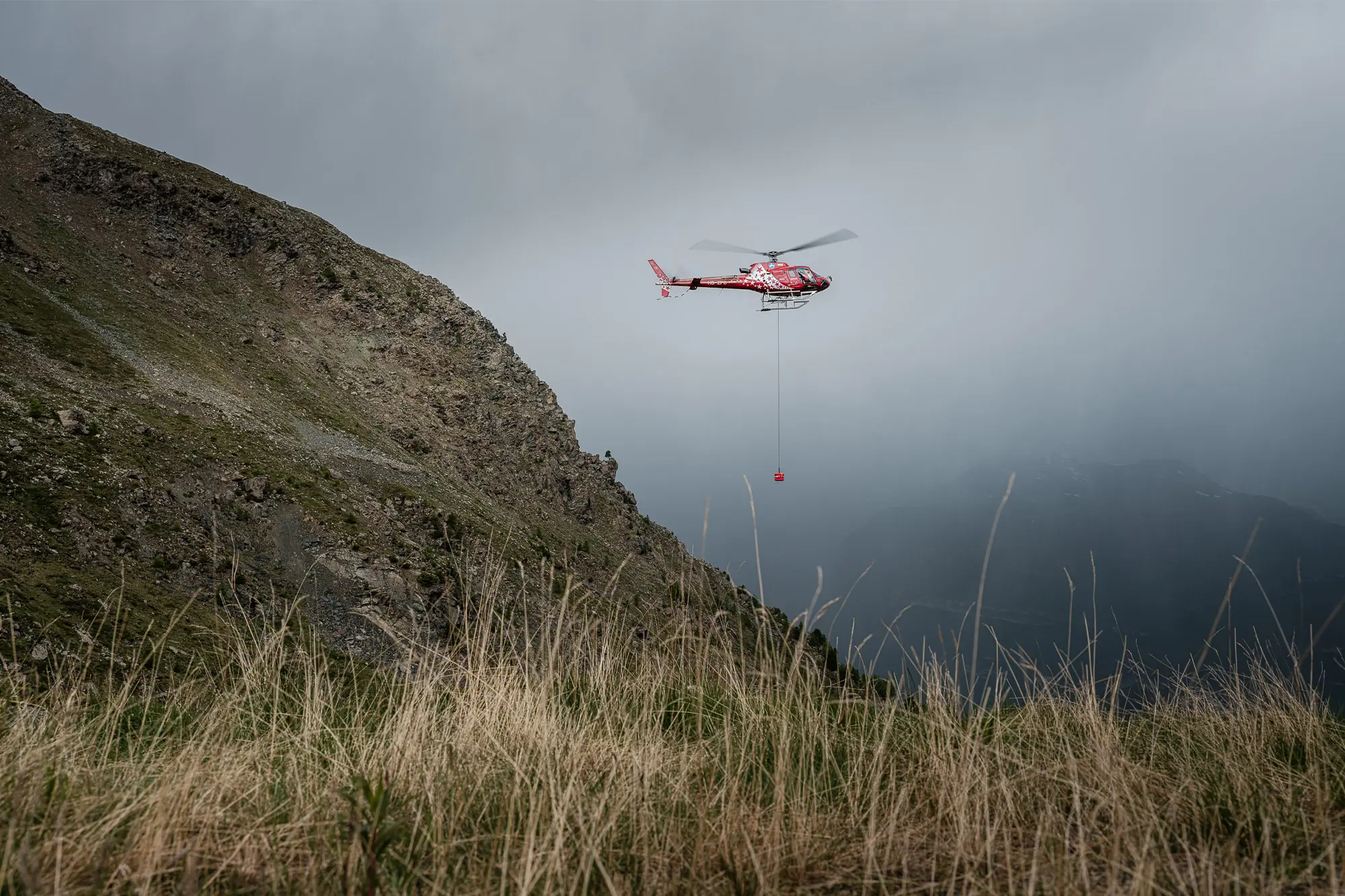 A RECCO helicopter flies near a mountain slope during search operations