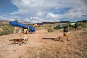Two people carry canoes above their heads in a desert like landscape
