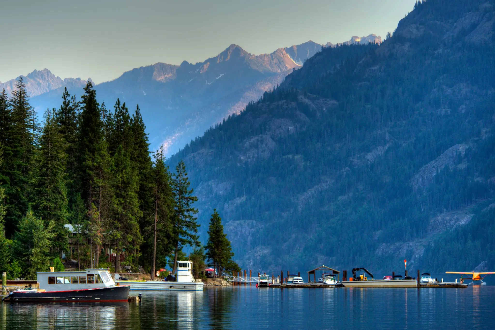 Multiple boats on a lake with trees on the left and mountains in the background