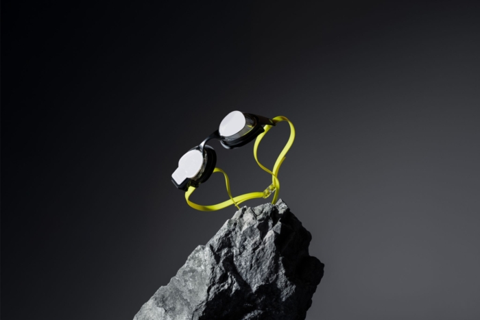 Black goggles with neon yellow strap in air over dark rock