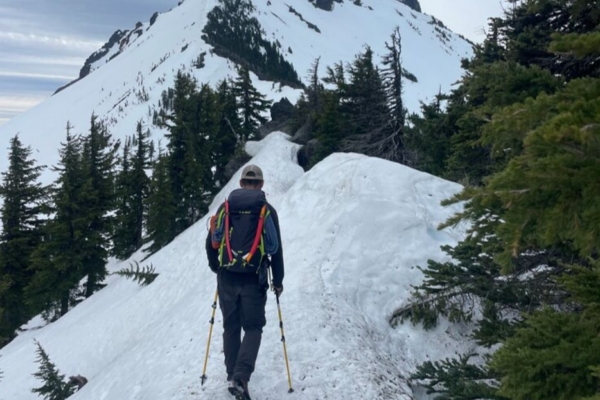 Man hikes along snow covered trail with mountain in background 