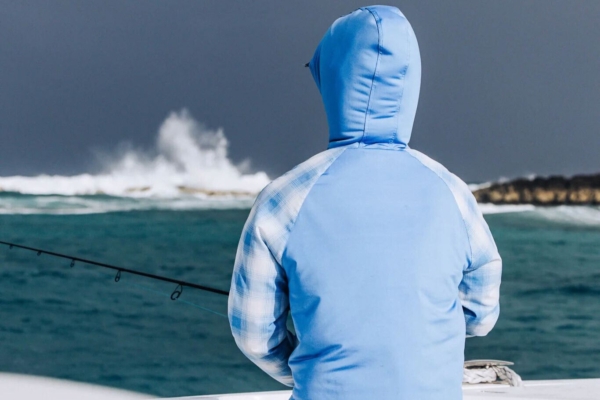 POV from behind seeing a man in a blue hoodie fishing on the ocean 
