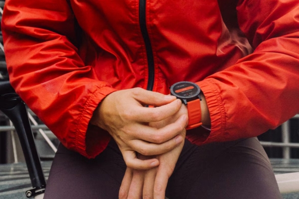 Close-up on the hands of a person wearing an orange jacket adjusting their smart watch