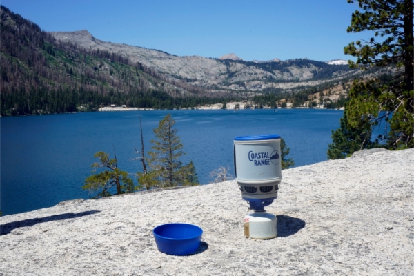 Stove set up on a rock with a lake and mountains in the distance
