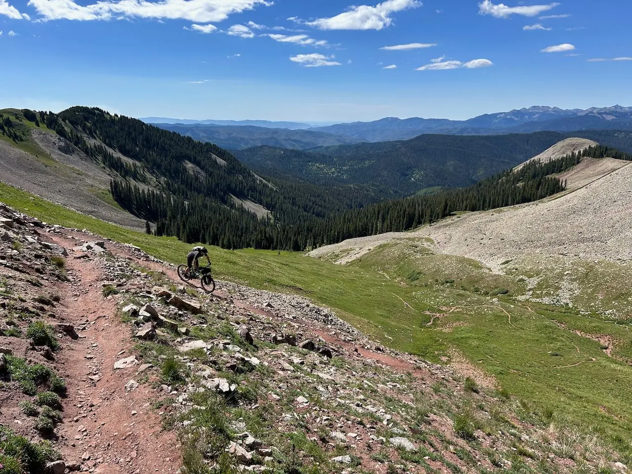 Rider descending a rocky trail on the Salsa Blackthorn 125 with a vast mountain backdrop