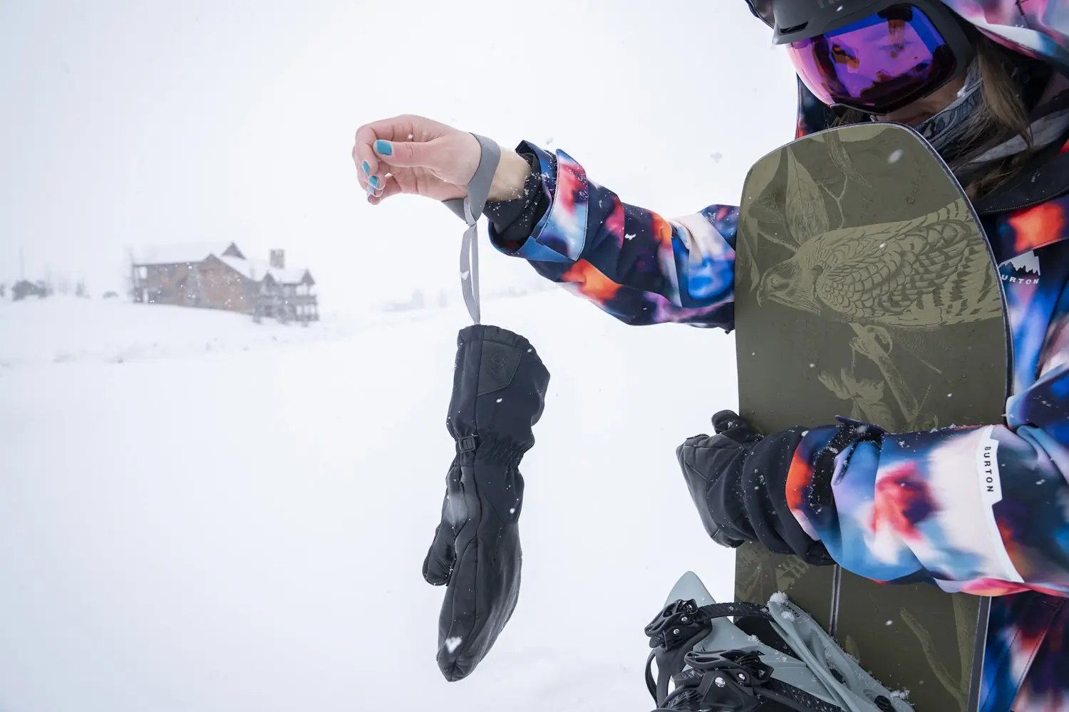 Close-up of a person wearing a colorful snow jacket and holding a Stio Objective Insulated Winter Mitten by its wrist leash