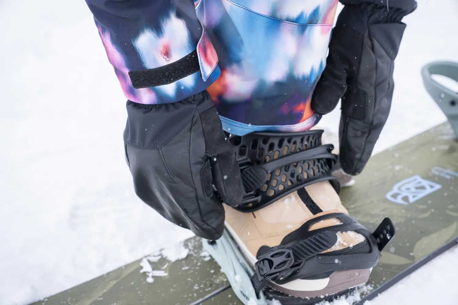 Person wearing Stio Objective Insulated Winter Mittens securing a snowboard binding in the snow.