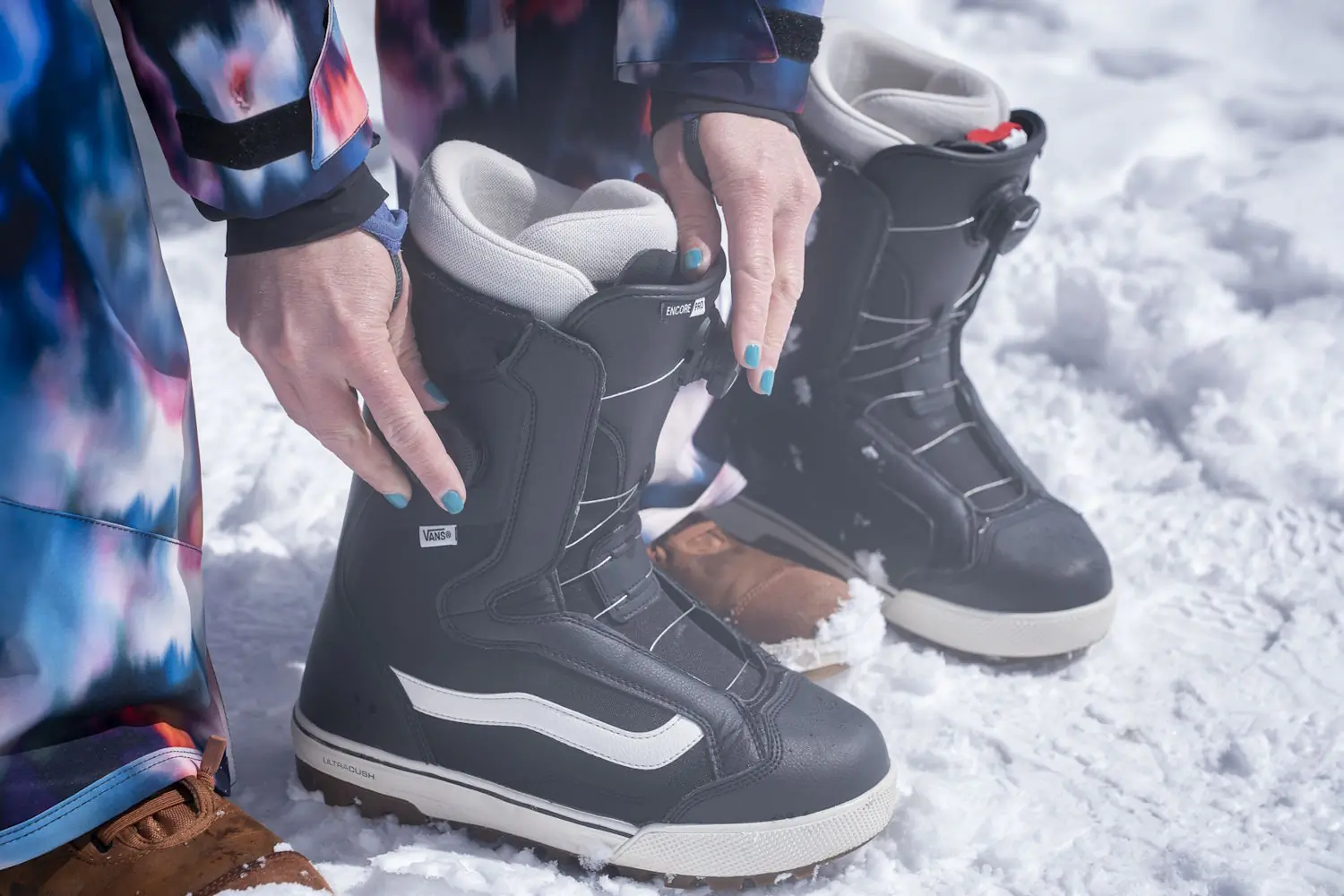 Woman adjusting Vans Women's Encore Pro Snowboard Boots on snowy ground.