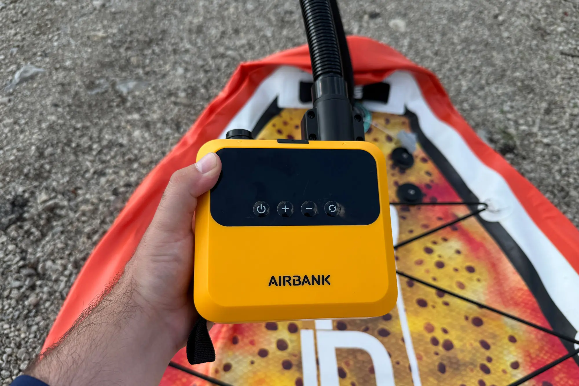 Hand holding the AIRBANK PULSE Pro Electric SUP Air Pump above the board
