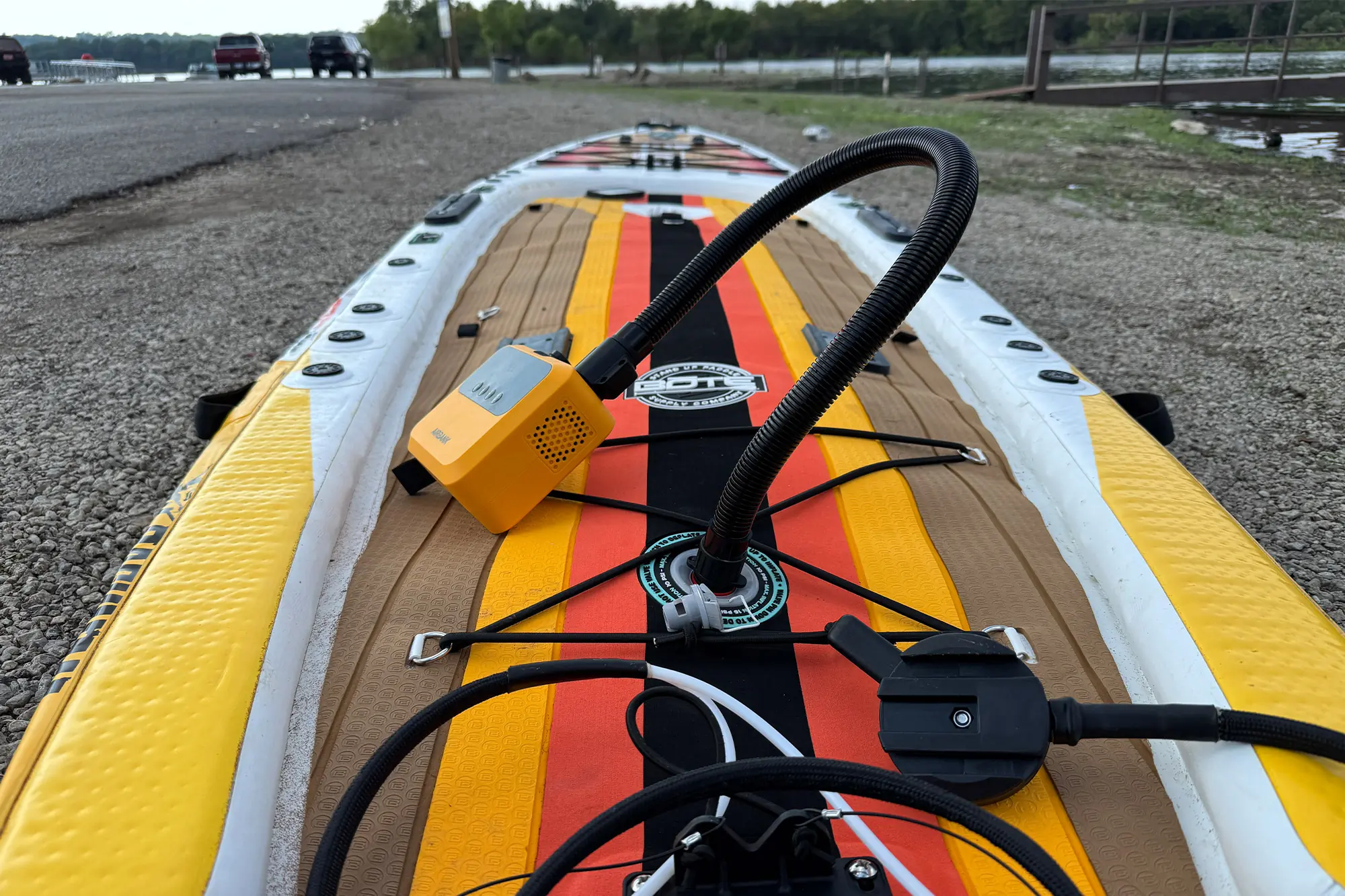 AIRBANK PULSE Pro Electric SUP Air Pump inflating a paddleboard on a lakeside launch area