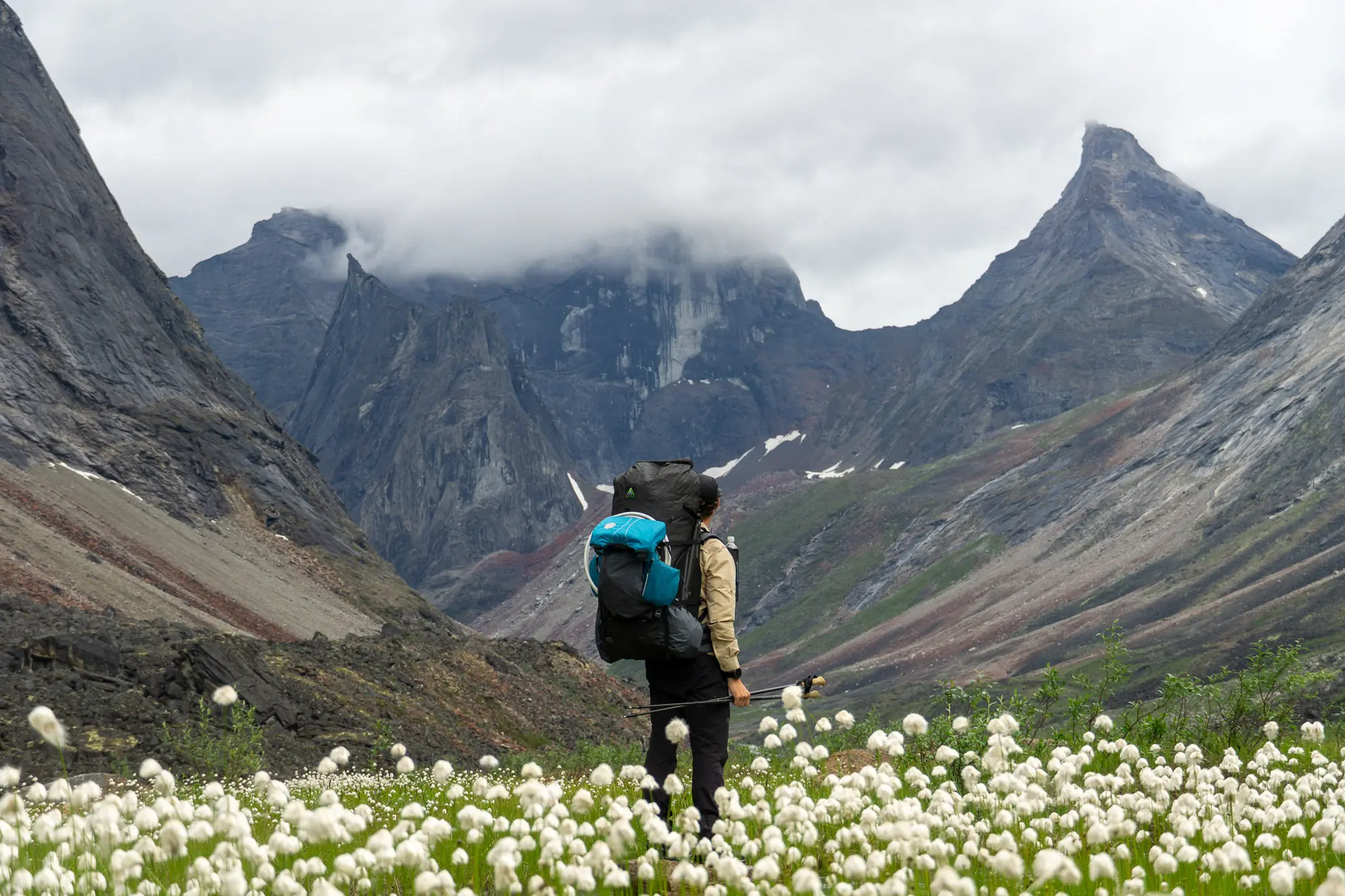 the author wearing an unaweep pack and standing in an alpine valley with arctic dandelions and large granite peaks in the background