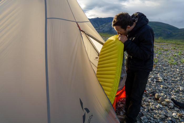 a backpacker in alaska inflates a yellow sleeping pad