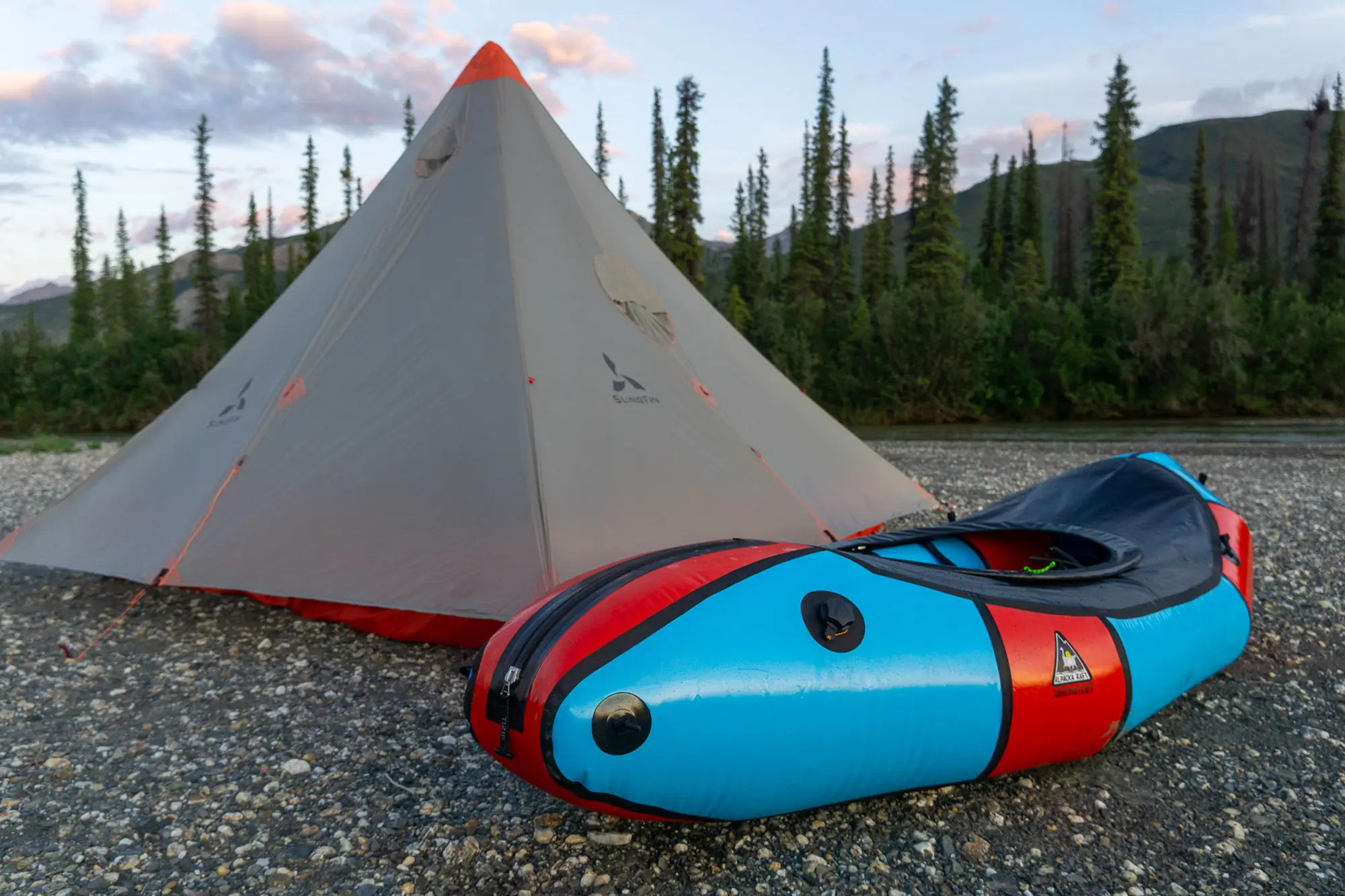 the slingfin cinder cone tarp set up on a river bar in alaska next to a red and blue packraft