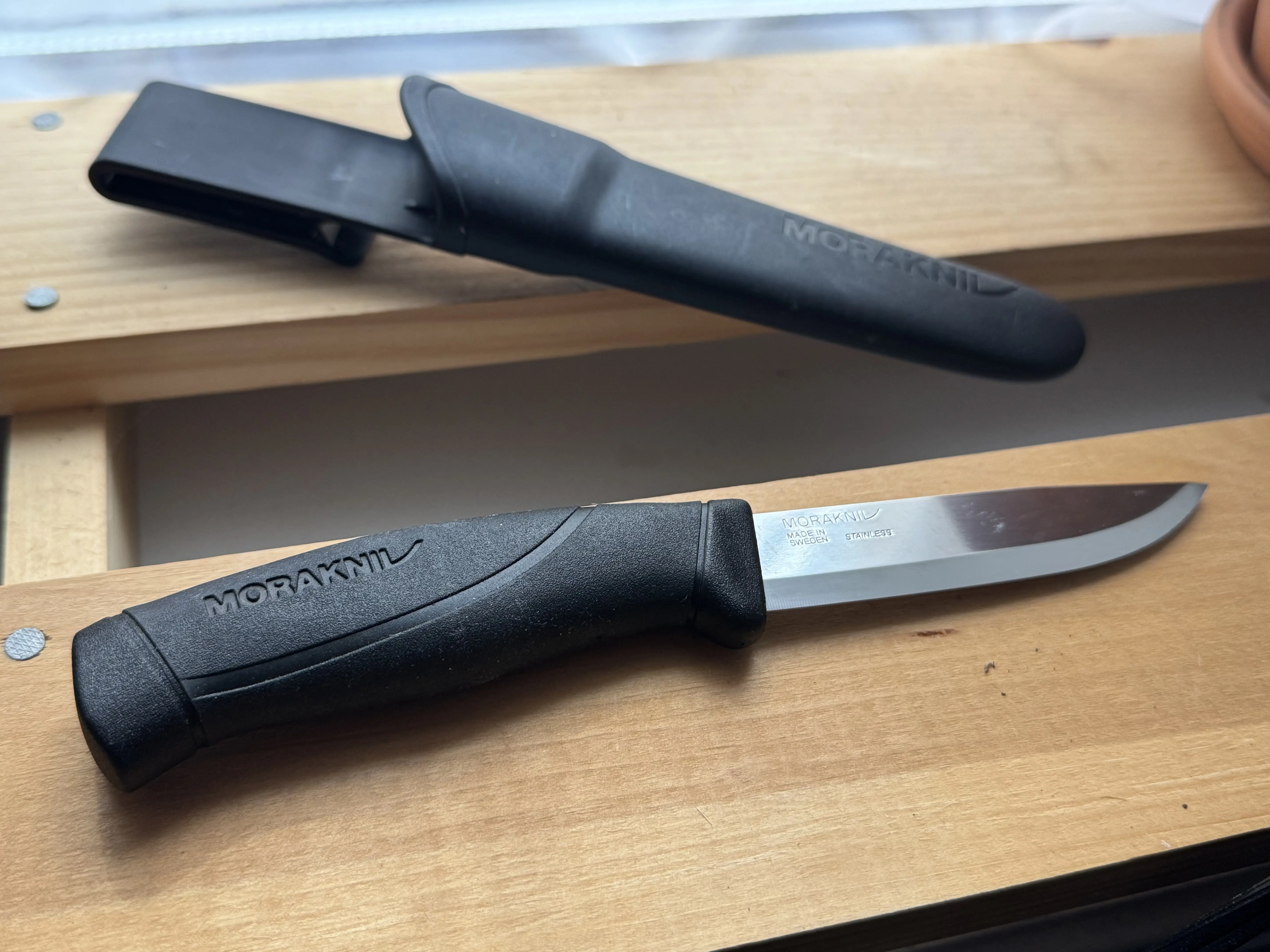 Morakniv Companion knife sitting on wood with its plastic sheath nearby
