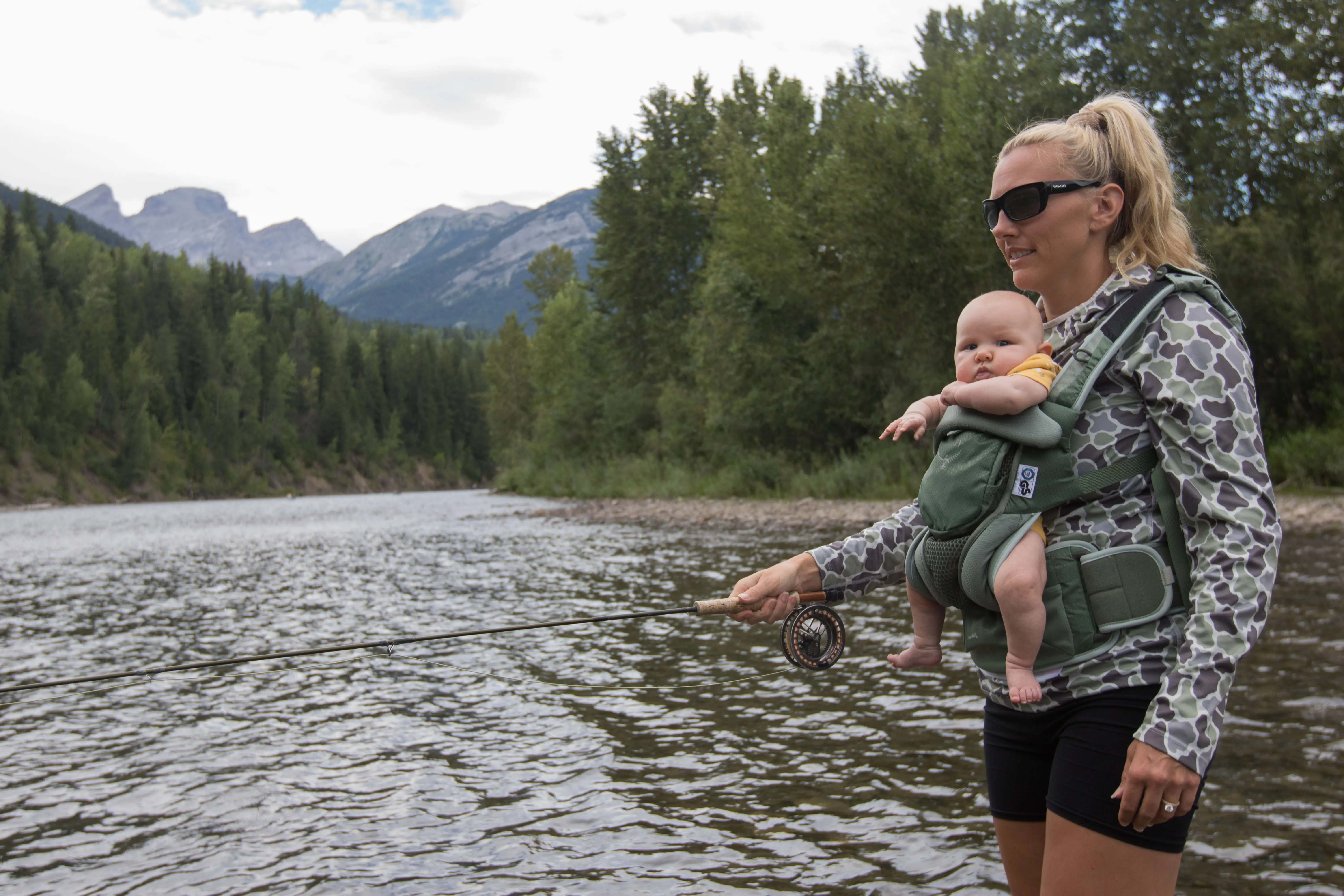 A woman fishing with a baby in a baby carrier
